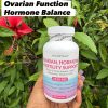 A bottle of Vita Optimal Ovarian, Hormone & Fertility Support, 120 capsules, held in front of a hibiscus plant
